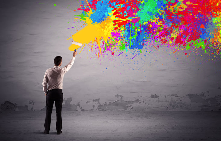 An elegant businessman in suit painting colorful splatter, bright colors on grey urban wall with a paint roller in his hand concept