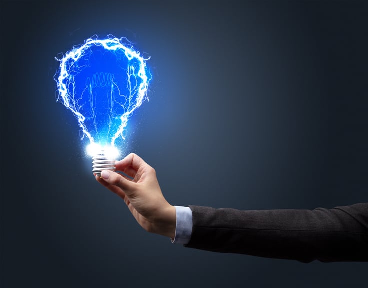 Hand holding shiny light bulb on dark background. New idea concept